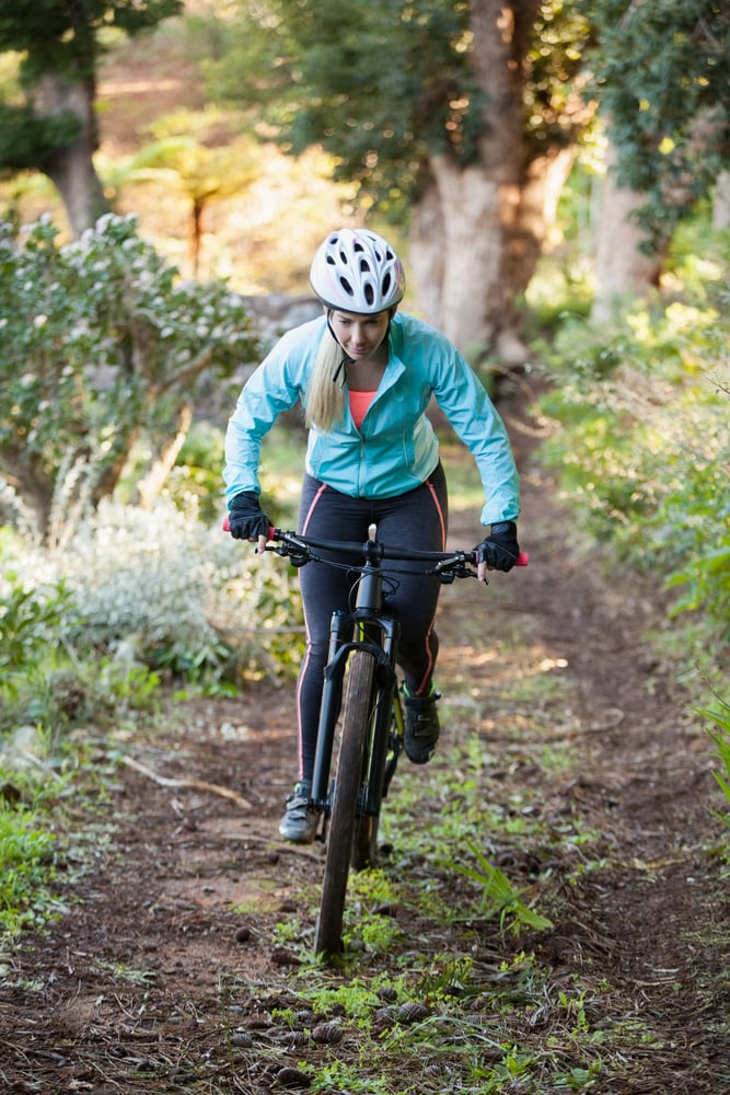 Female mountain biker riding bicycle in the forest on a sunny day